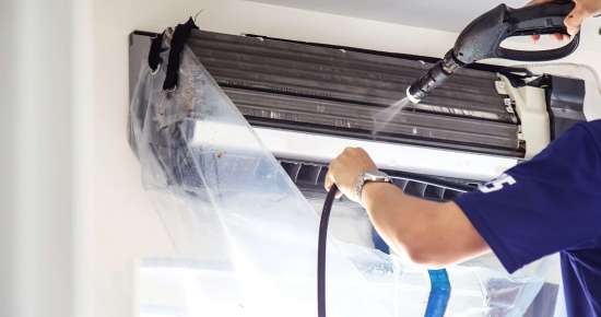The technicians are cleaning the air conditioner by spraying water. Hand and water spray are cleaning the air conditioner on white background.